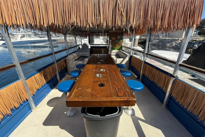 Inside a tiki-style boat with a long wooden table and blue stools.